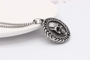 Close-up of vintage skull pendant with 3D relief and textured oval frame on steel chain