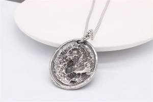 Macro shot of silver oval pendant featuring unique vintage rock texture and aged finish