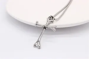 Close-up of vintage bone cross pendant on a round snake chain over white ceramic