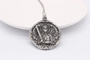 Macro detail of vintage steel necklace showing embossed winged angel with sword and cross