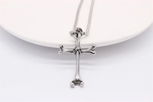 Close-up of retro silver bone cross pendant with vintage oxidized texture on white plate
