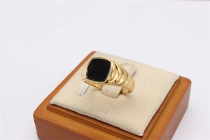 Detailaufnahme eines vergoldeten Titanrings mit schwarzer Onyx-Einlage auf einem Holzständer