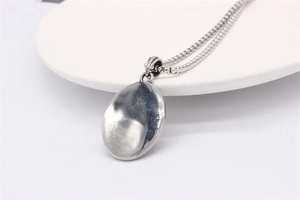 Macro detail of polished silver oval pendant with reflective mirror surface on ball chain