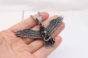 Detailed view of a vintage stainless steel eagle and snake pendant held by hand