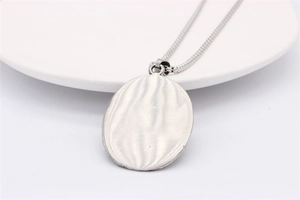 Détail d'un pendentif ovale argenté aux textures ondulées sur une assiette en céramique