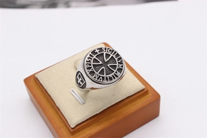 Detail of vintage silver cross signet ring with engraved Latin text on beige stand