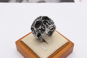 Close-up of vintage steel skull ring with cratered texture on a beige jewelry display
