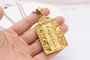 Detail showing hand holding a golden Buddhist Vajra pendant with ornate cloud patterns
