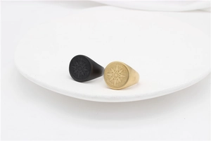 Detail view of matte black and gold compass signet rings in a white ceramic tray