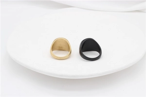 Macro detail of matte finish signet rings in gold and black on a white ceramic tray