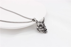 Detailed view of vintage silver Hannya skull pendant with box chain on ceramic