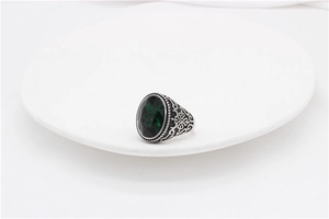 Macro shot of silver titanium steel ring with green oval gemstone and floral engraving