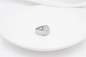 Detail of silver prayer hands signet ring with engraved religious text on white ceramic