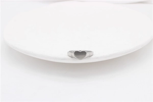 Macro detail of a silver heart signet ring on a clean white minimalist display stand