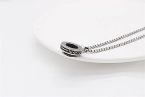 Detail view of retro silver pendant necklace with carved patterns on a white ceramic plate