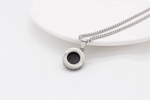 Detailed view of silver box chain and round pendant with black gemstone inlay