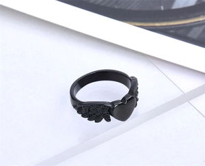 Detail view of black heart ring with angel wings on a minimalist white background