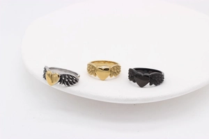Three angel wing heart rings in gold, silver, and matte black finish on a white tray