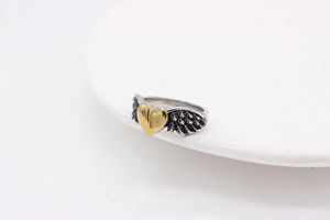 Detail of vintage angel wings ring with a gold heart center on a silver steel band