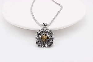 Detailed close-up of retro compass star pendant on a snake chain over a stone tray