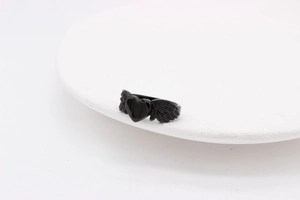 Detailed close-up of a black heart ring with angel wings on a white ceramic plate
