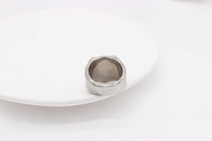 Detailed view of wide polished silver stainless steel ring band on white ceramic plate