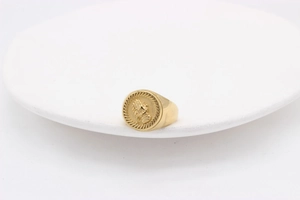 Détail macro d'une bague chevalière dorée montrant le relief des mains en prière