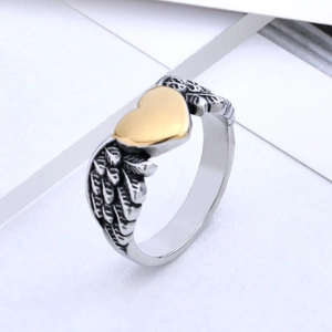 Minimalist two-tone steel ring with gold heart and silver angel wings on white pedestal