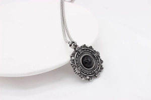 Detail of gothic silver tag necklace featuring a round black gemstone and baroque floral relief
