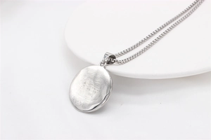 Detail of round silver pendant with hammered texture and beaded chain on ceramic tray