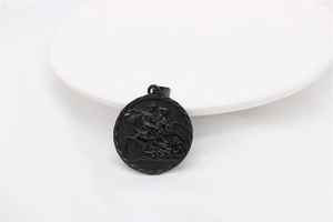 Detailed close-up of matte black St. George and the Dragon relief on a round steel pendant