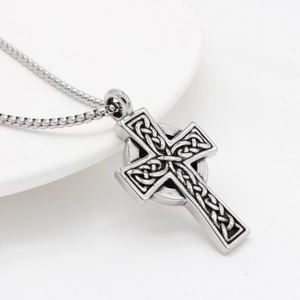 Vintage silver Celtic cross pendant necklace with intricate knot texture on white plate
