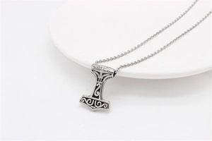 Macro shot of silver Thor's Hammer Mjölnir pendant with vintage floral engravings on a chain