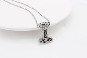 Close-up of a vintage Mjolnir pendant with Viking relief on a white ceramic plate