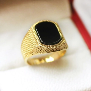 Makro-Detail eines Herrenrings in Gold mit schwarzem Edelstein und strukturierter Fassung