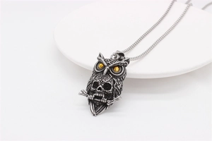 Detail of owl skull pendant with yellow eyes and vintage silver finish on white ceramic