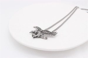 Detailed close-up of retro eagle pendant with box chain on a white ceramic tray