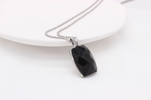 Détail macro du pendentif rectangulaire en pierre noire sur une chaîne argentée polie