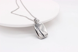 Détail d'un pendentif rectangulaire argenté incurvé avec une finition miroir polie
