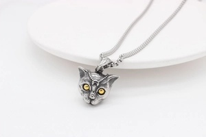 Macro detail of retro silver cat head pendant with yellow eyes on white ceramic tray