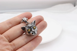 Macro shot of a vintage punk cat head pendant with yellow eyes and silver texture