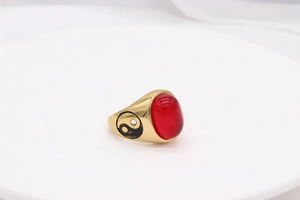 Detailed macro view of gold-plated ring with red oval gemstone and yin-yang carving