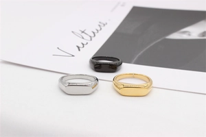 Trois chevalières minimalistes en argent, or et noir posées sur un fond de tissu blanc épuré
