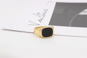 Détail d'une bague chevalière minimaliste dorée avec un insert rectangulaire en émail noir