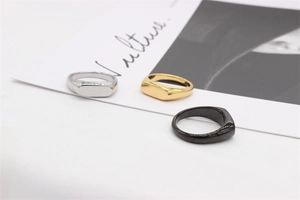 Trois chevalières minimalistes en or, argent et noir sur un fond de magazine de mode