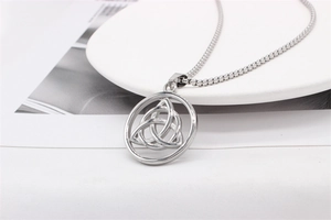 Macro shot of silver Triquetra Celtic knot pendant on bead chain against a white plate