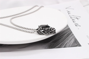 Detail of vintage silver dragon pendant with black gemstone on a steel box chain