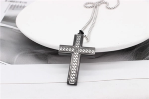 Detailed close-up of a two-tone cross pendant with woven relief and steel chain necklace