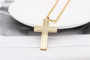 Close-up of golden cross pendant necklace with leaf texture and small zircon stone