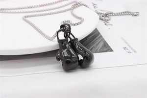 Close-up of black boxing glove pendant with silver chain on a white ceramic tray